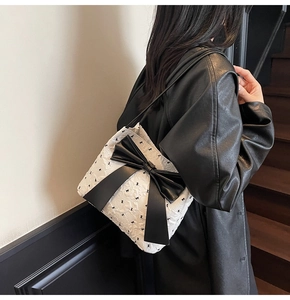 Detail of white pleated tote with large black bow on a model wearing a leather coat