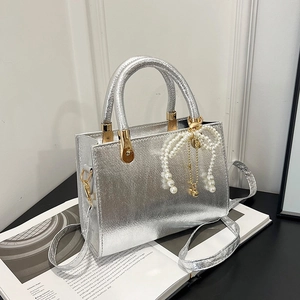 Silver metallic rectangular crossbody bag with pearl bow charm on an open magazine