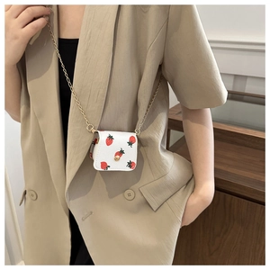 Mini strawberry print crossbody bag with gold chain strap worn on a beige blazer
