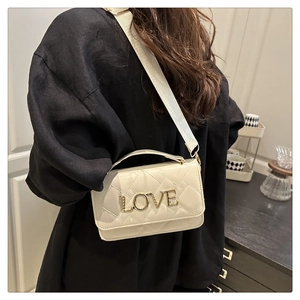 Détail du sac bandoulière matelassé crème avec lettrage LOVE doré sur vêtement noir