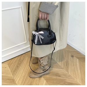 Detail of black leather handbag with delicate pink lace bow and adjustable shoulder strap