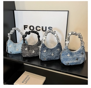Detail view of denim dumpling bags with butterfly accents and metallic handles in four colors