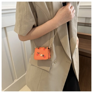 Close-up of a mini orange crossbody bag with strawberry print and gold chain strap