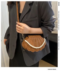 Detail of brown shell-shaped crossbody bag with crocodile pattern and pearl handle
