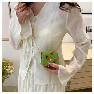 Litchi pattern green cherry print wallet bag shown with gold chain on white outfit