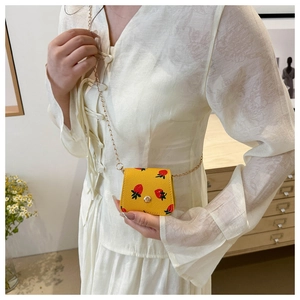 Detailed view of mini yellow strawberry crossbody bag with gold chain strap on model