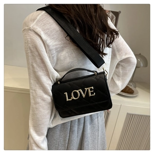 Model showing a black quilted crossbody bag with a gold LOVE buckle and wide strap