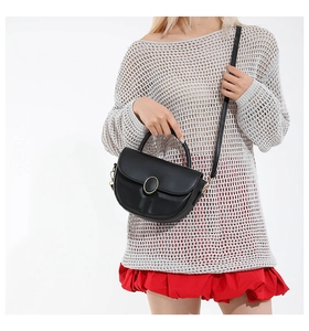 Detail of a matte black saddle bag with golden oval buckle and adjustable shoulder strap
