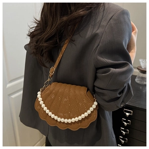 Brown shell-shaped crossbody bag with pearl chain detail worn by a model in a gray suit