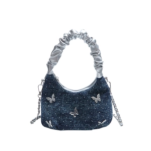 Blue denim crossbody bag with silver butterfly charms and ruffled handle on white background
