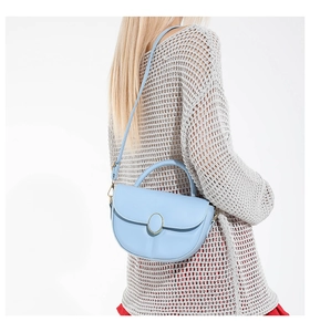 Detail of light blue saddle bag with gold metal clasp on a knitted texture