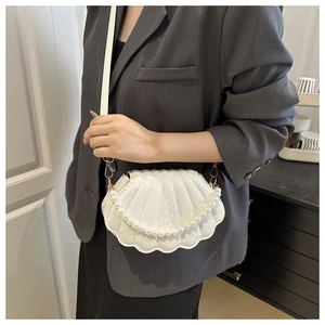 Detail of white shell-shaped crossbody bag featuring pearl handle and embossed leather texture