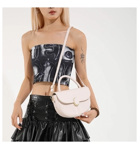 Detail of a chic cream saddle bag with gold oval buckle and thin adjustable strap