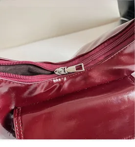 Detail of smooth silver zipper on wine red patent leather tote bag with glossy finish