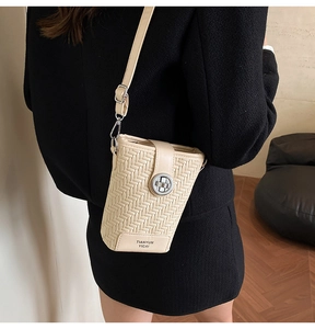 Detail of woven texture and silver metallic buckle on cream-white PU leather bucket bag