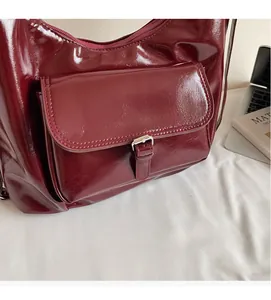 Detail of dark red glossy shoulder bag with buckle pocket and smooth zipper closure