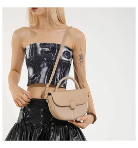 Detail of a beige saddle bag with gold oval buckle and top handle worn by a model