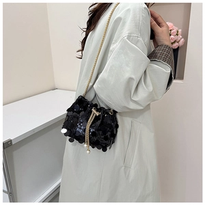 Detail of black sequin bucket bag with gold chain strap and pearl drawstring on model
