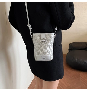 Detail of silver woven crossbody bag with round metal clasp worn by a fashion model