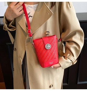 Detail shot of a vibrant red woven crossbody bag featuring a silver twist lock closure