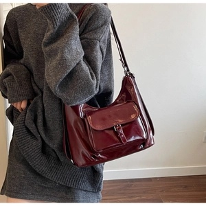 Gros plan du sac hobo en cuir verni bordeaux brillant avec boucle métallique et bandoulière chic