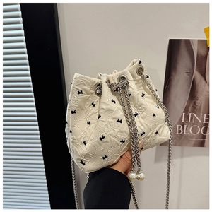 Detail of cream drawstring bucket bag with textured pleats and pearl charm accents