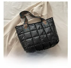 Detail of black quilted tote bag with woven handles shown next to a smartphone for scale