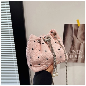Close-up of pink bow-patterned bucket bag with pearl drawstring and silver chain strap