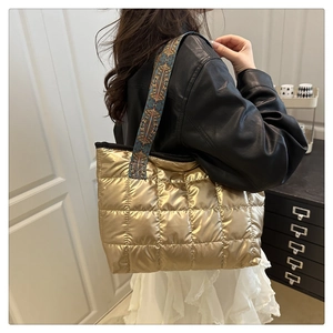 Detail of gold quilted down tote bag featuring colorful ethnic embroidered wide strap