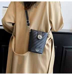 Detail of black woven crossbody bucket bag with silver metal lock on khaki coat