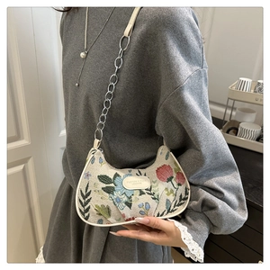 Détail de broderie florale et chaîne en métal sur le sac bandoulière beige demi-lune