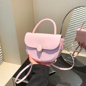 Pink leather saddle handbag with gold metal clasp and adjustable strap in cozy room setting