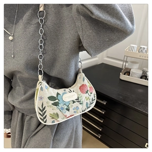 Détail d'un sac sous le bras en tapisserie florale avec chaîne argentée porté par un mannequin