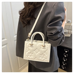 Detail of white embossed handbag with floral texture worn by model in grey blazer