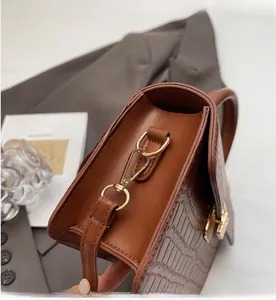 Detailed close-up of golden metal clasp and crocodile pattern on brown handbag