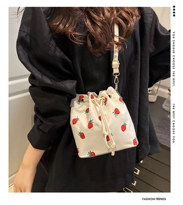 Detail of strawberry print bucket bag featuring drawstring closure and gold hardware