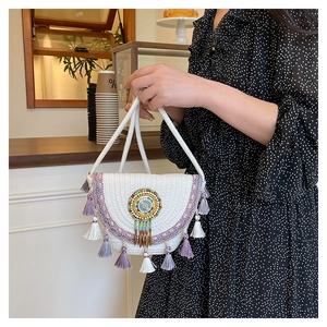 Detail of woven straw shoulder bag featuring purple ethnic embroidery and hanging tassels