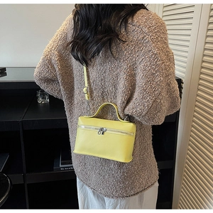 Detail view of a bright yellow box bag with pebble texture and top handle on a model
