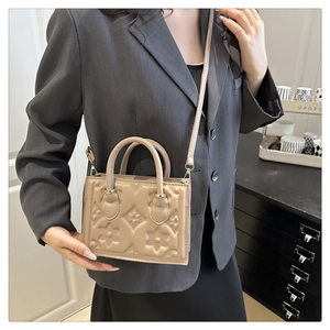 Detail of beige small square bag with floral embossed patterns and metal hardware
