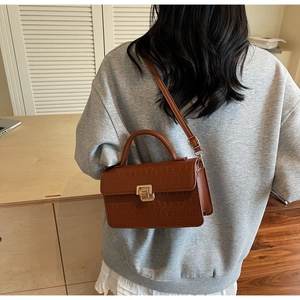 Detail of a brown crocodile pattern shoulder bag with a polished golden metal lock buckle