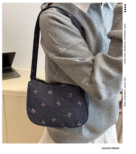 Detail of blue denim crescent bag with colorful butterfly embroidery and logo lettering