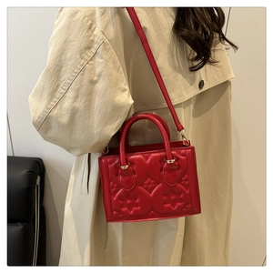 Red quilted square handbag with floral texture worn over a beige trench coat