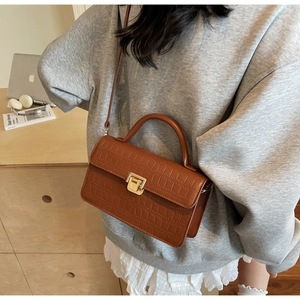 Detail of caramel crocodile embossed leather bag with gold clasp and top handle