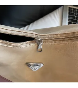 Detail of silver smooth zipper and triangular metal logo on beige nylon tote bag