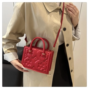 Close-up of a red embossed floral small square bag carried by a model in a trench coat