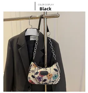 Détail de broderie florale sur sac beige avec bandoulière en cuir noir et chaîne
