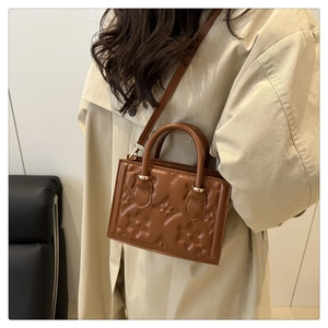 Detail of embossed floral pattern on caramel brown crossbody bag with top handles