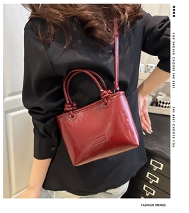 Detail of a dark red glossy crossbody tote bag with a mirror finish and knot handle