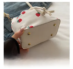 Detail view of gold-tone bottom studs and strawberry print on a canvas bucket bag
