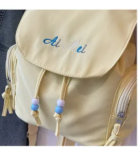 Detail of light yellow backpack showing refined embroidery and colorful beaded drawstrings
